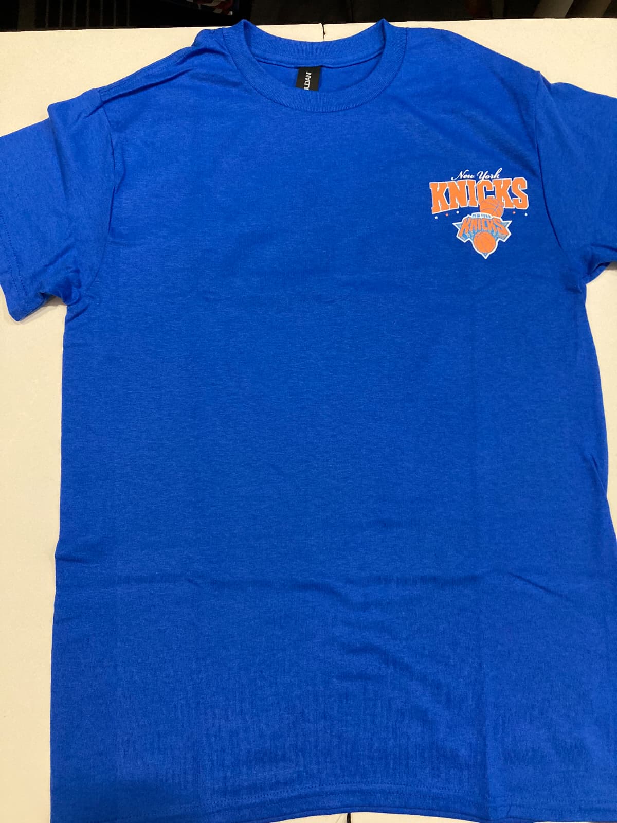 Blue t-shirt with a New York Knicks logo on a beige background, front view, rount neck t-shirt